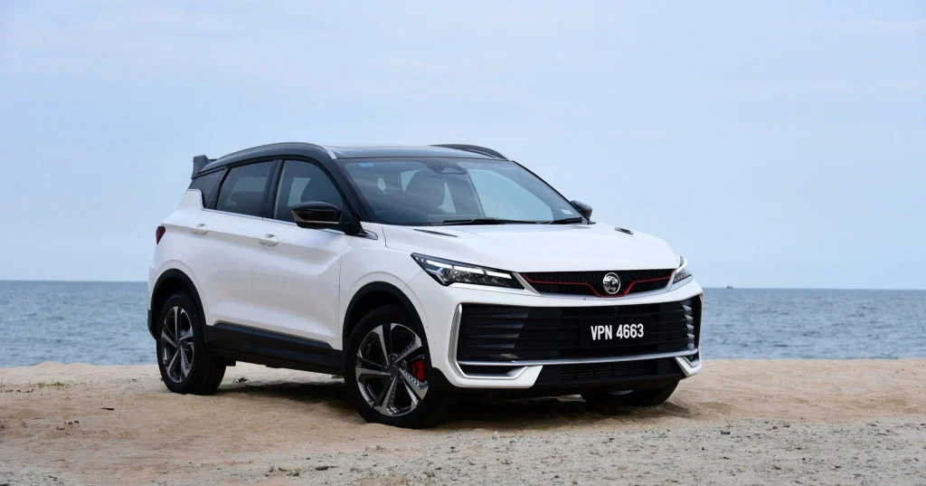 Proton X50 berwarna putih diparkir di tepi pantai dengan latar laut dan langit cerah